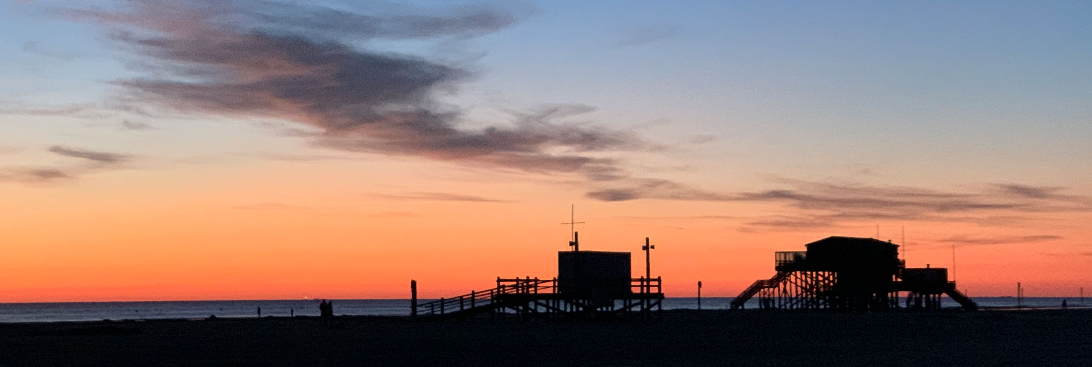 Abendrot über der Nordsee mit Pfahlbauten am Strand